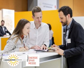 Beratungssymbol bei der Energiesparmesse Wels: Berater des OÖ Energiesparverbandes im Gespräch mit einem jungen Paar; links unten das Logo des Energiesparverbandes und das der Energiesparmesse Wels